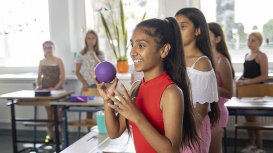 eine Schüler*innengruppe, im Vordergrund ein Mädchen das einen Ball wirft