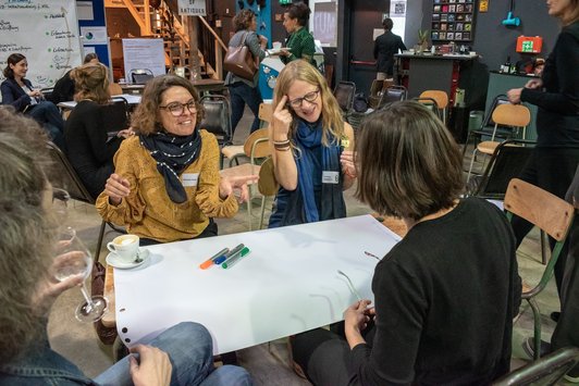 vier Teilnehmer sitzen als Gruppe auf einem alten Schultisch und arbeiten zusammen