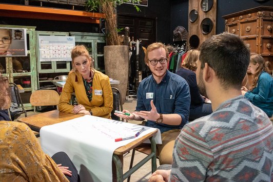 Teilnehmer sitzen als Gruppe auf einem alten Schultisch und arbeiten zusammen