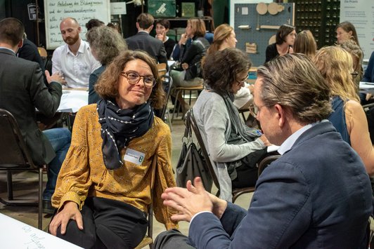 Teilnehmer sitzen als Gruppe auf einem alten Schultisch und arbeiten zusammen