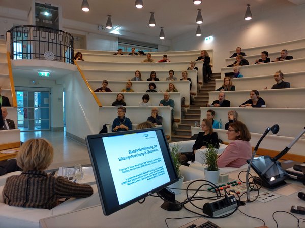 Menschen sitzen in einem Hörsaal der Uni Wien und hören sich die Studienpräsentation zur Bildungsforschung in Österreich an.