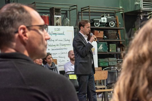 Jakob Calice eröffnet mit Mikrofon in der Hand die Veranstaltung mit einer Begrüßungsrede