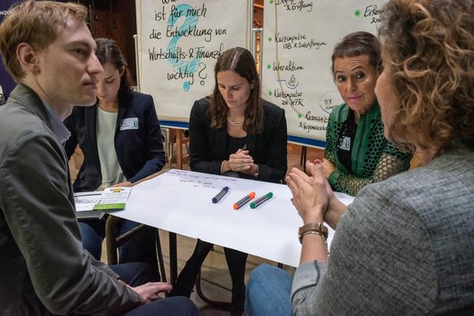 Teilnehmer sitzen als Gruppe auf einem alten Schultisch und arbeiten zusammen